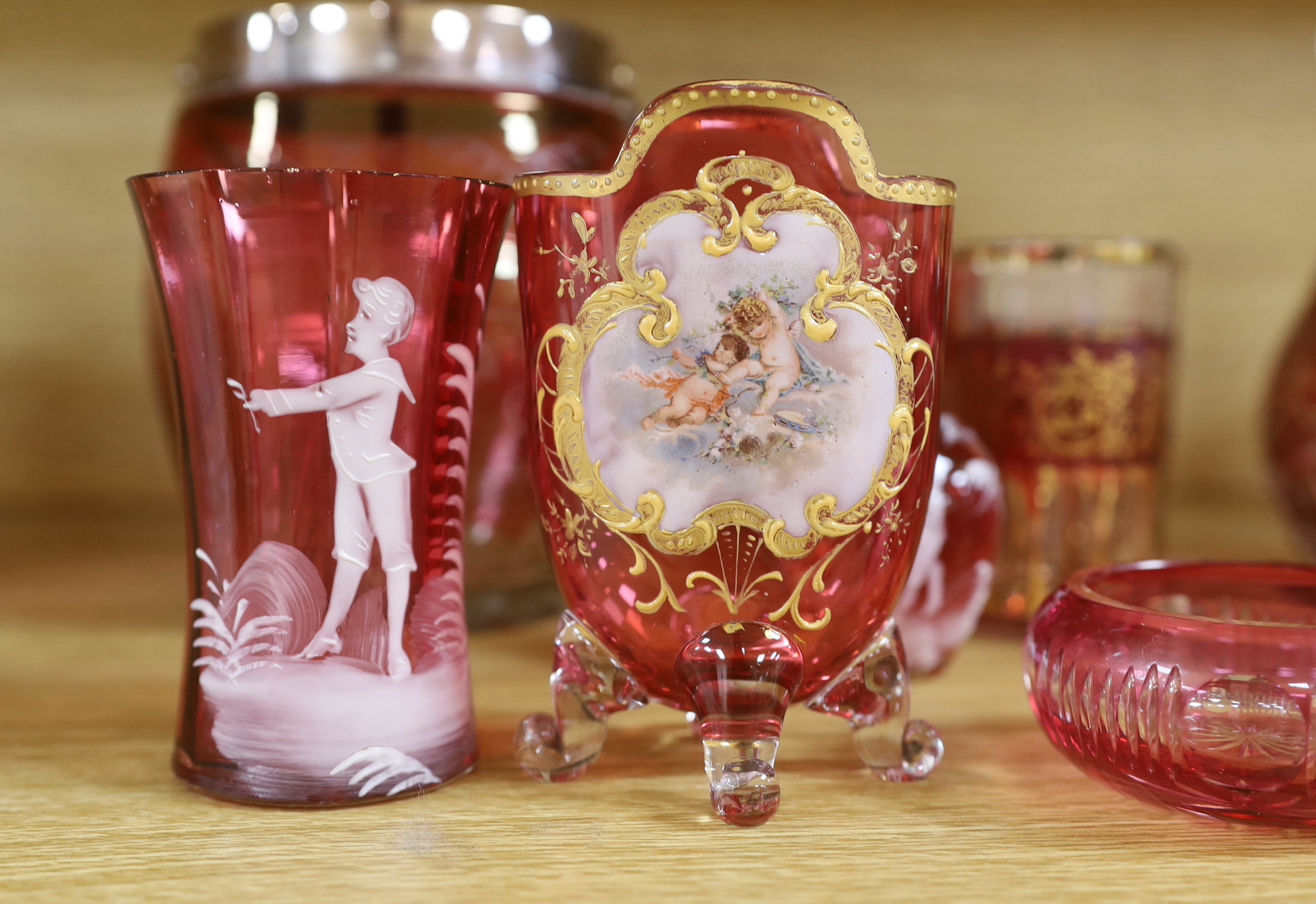 Antique and later cranberry glassware including a biscuit barrel etched with grapevines, Mary Gregory beakers and scent bottle and a vase with enamelled and gilt decoration, the largest 21cm high